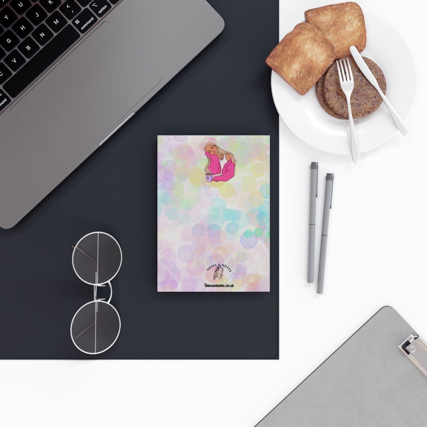 Vibrant colorful hardback journal on a black surface with glasses and pens nearby.