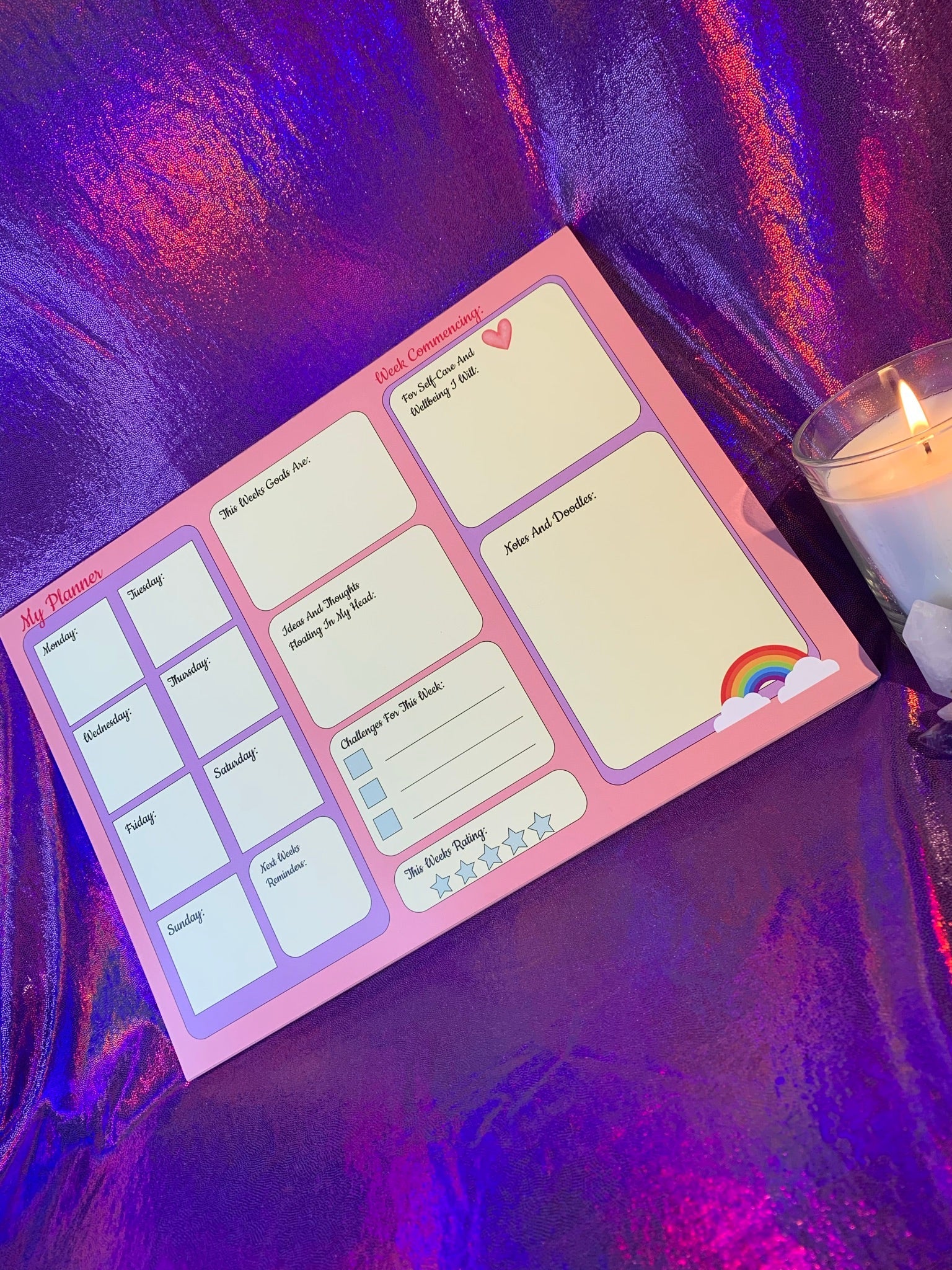 The Pretty in Pink A4 Desk Planner on a purple surface with candle nearby.