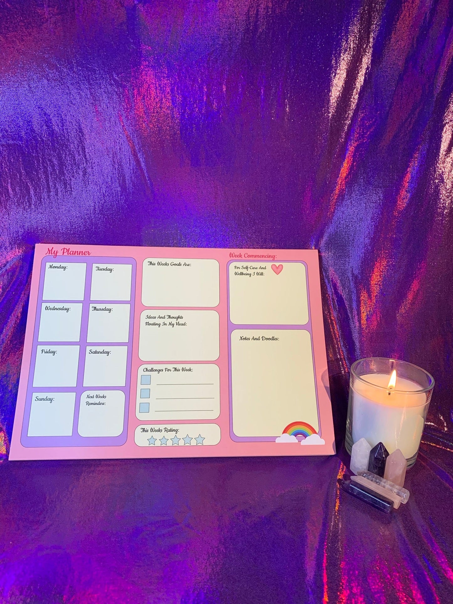 The Pretty in Pink A4 Desk Planner with colorful sections on a purple background, accompanied by a candle and crystals.