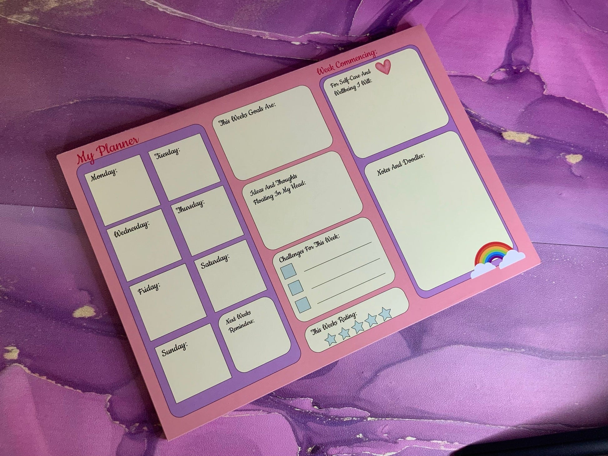 The Pretty in Pink A4 Desk Planner on a purple marbled background with sections for organizing weekly plans and notes.