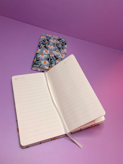 A6 embroidered daisy hardback notebook with lined pages open on purple surface