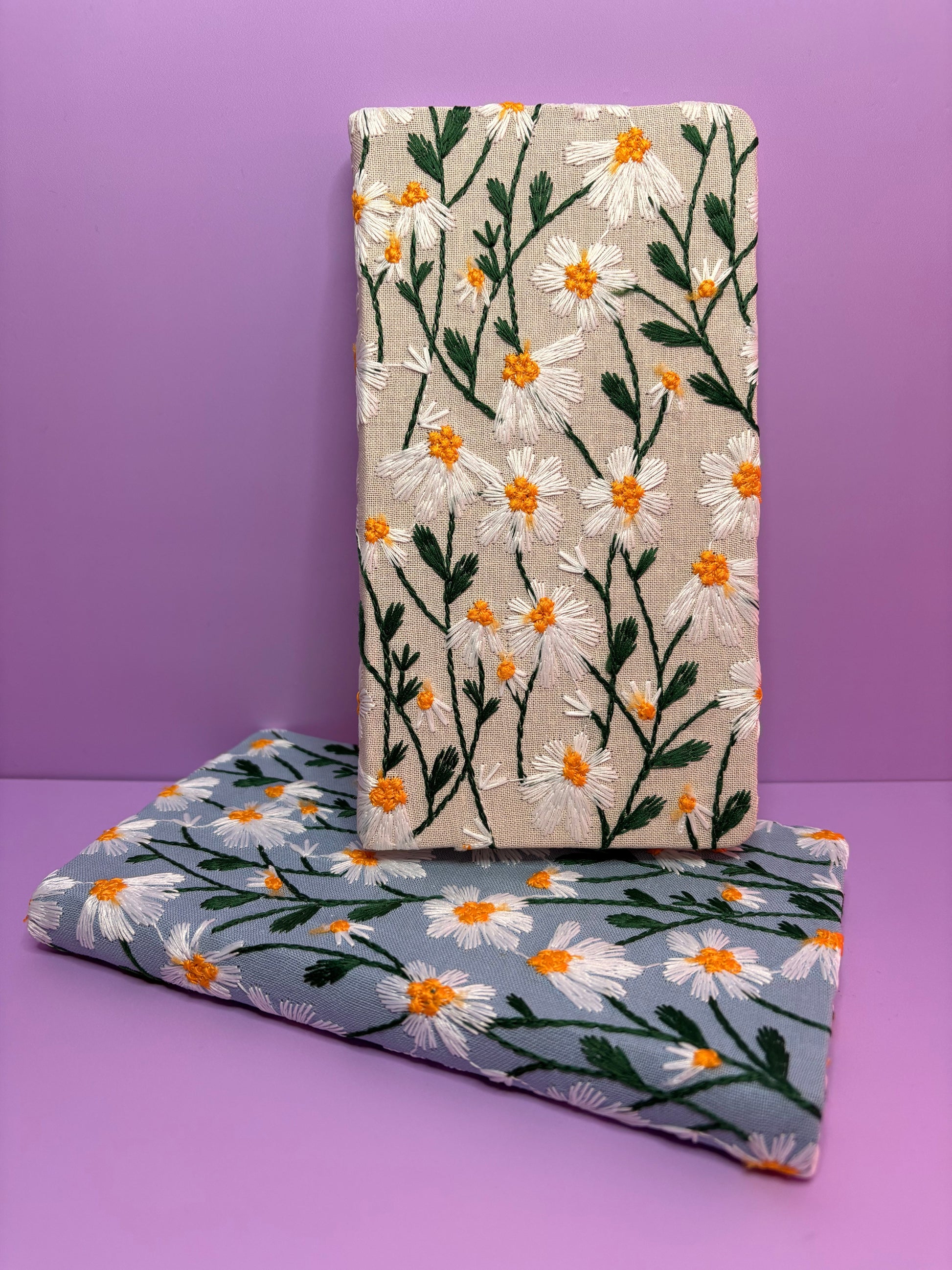 A6 embroidered daisy floral notebook in cream and blue hardback covers on purple background