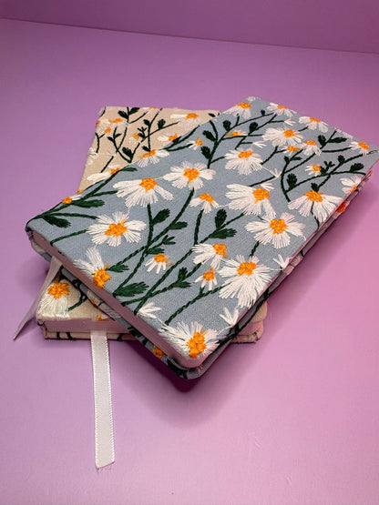 A6 embroidered daisy notebooks with hardback covers in blue and cream floral designs on a purple background