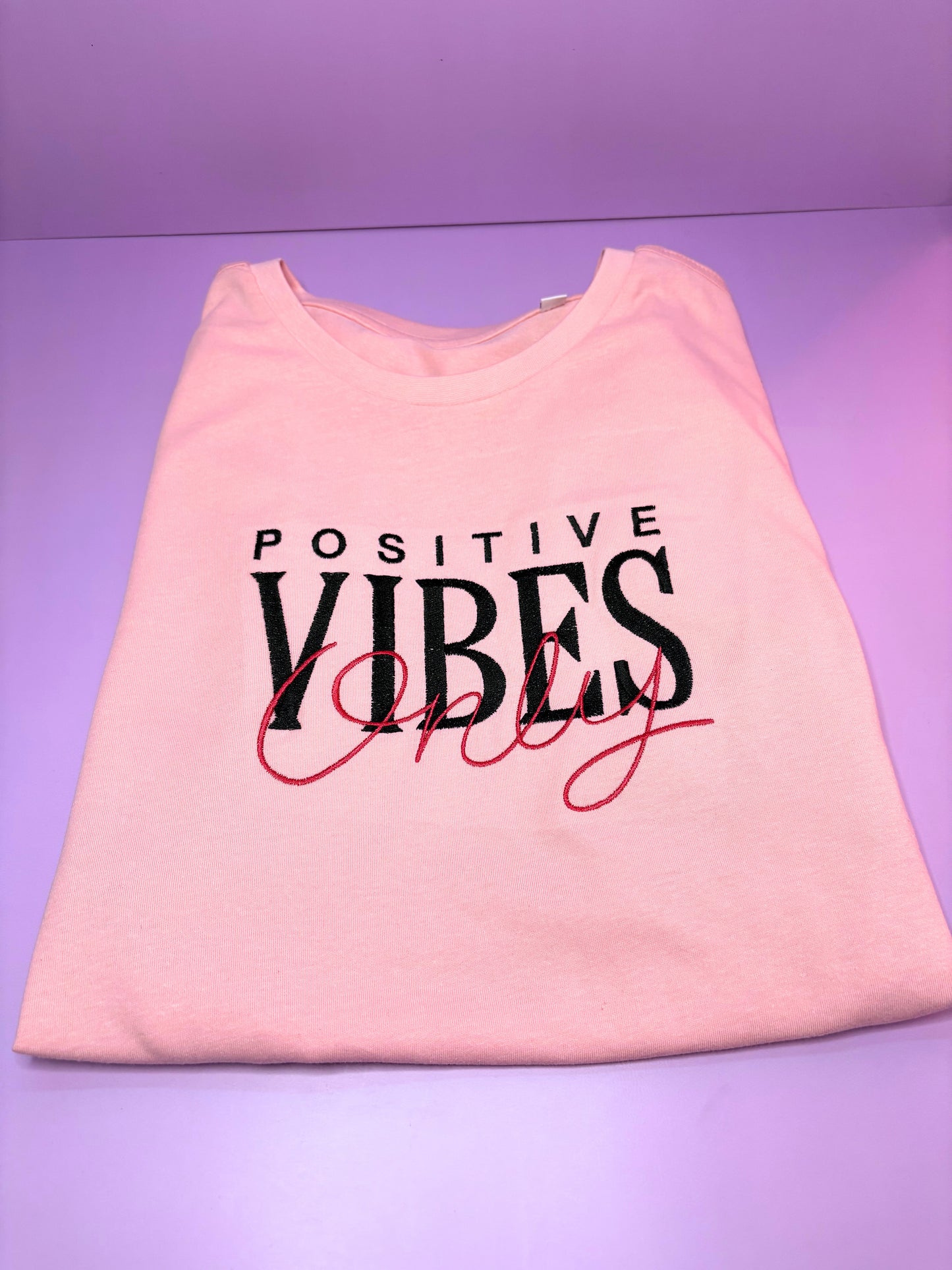 Baby pink short sleeve t-shirt with embroidered "Positive Vibes Only" text, ribbed crew neck, relaxed fit.