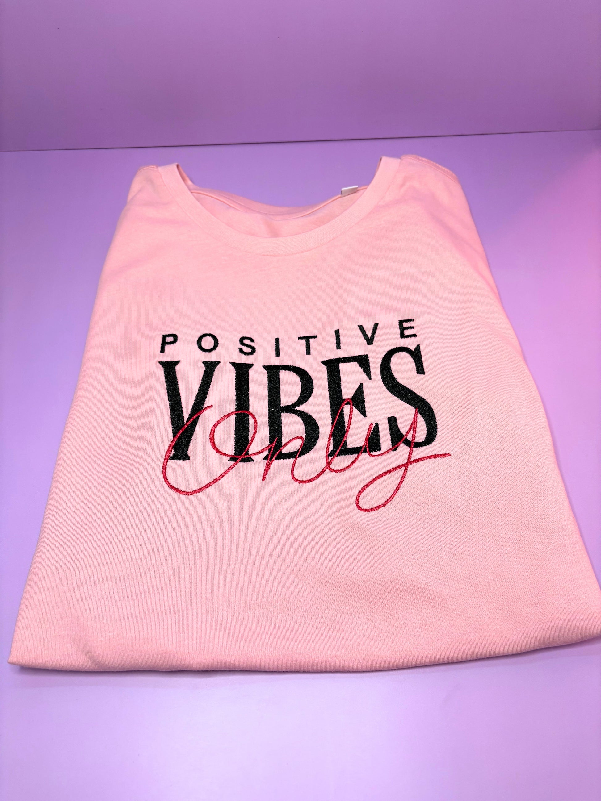 Baby pink short sleeve t-shirt with embroidered "Positive Vibes Only" text, ribbed crew neck, relaxed fit.