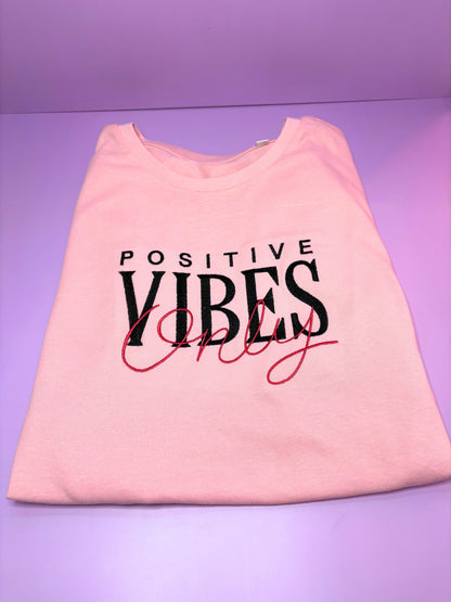 Baby pink short sleeve t-shirt with embroidered "Positive Vibes Only" text, ribbed crew neck, relaxed fit.