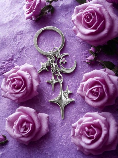 3D metal alloy silver celestial moon and stars keychain surrounded by purple roses on a textured purple surface
