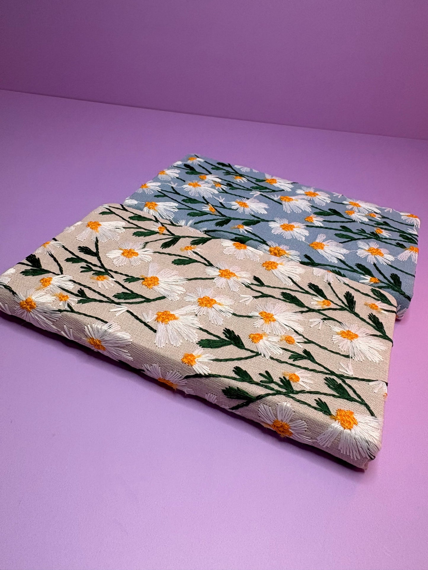 A6 embroidered daisy notebooks with blue and cream hardback covers on purple background