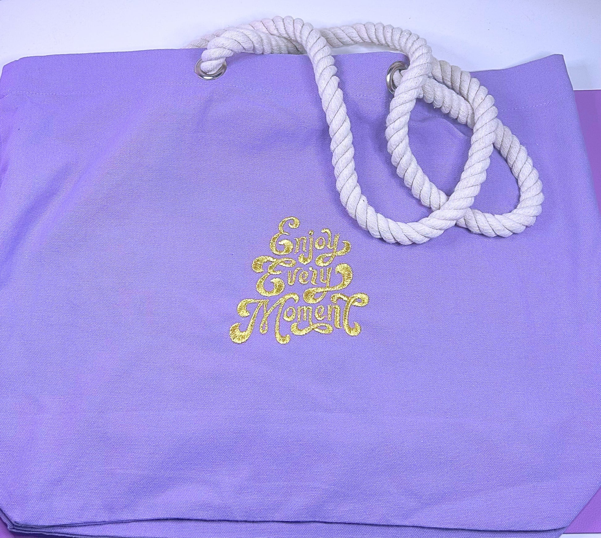 Lilac marine style tote bag with twisted rope handles and "Enjoy Every Moment" embroidered in gold thread.