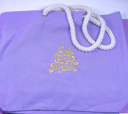Lilac marine style tote bag with twisted rope handles and "Enjoy Every Moment" embroidered in gold thread.