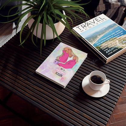Colourful hardback journal with vibrant design on a coffee table, surrounded by a plant, travel magazine, and coffee cup.