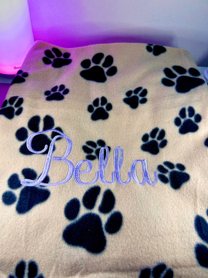 Personalised dog blanket with paw prints and custom name embroidery in soft fleece fabric.