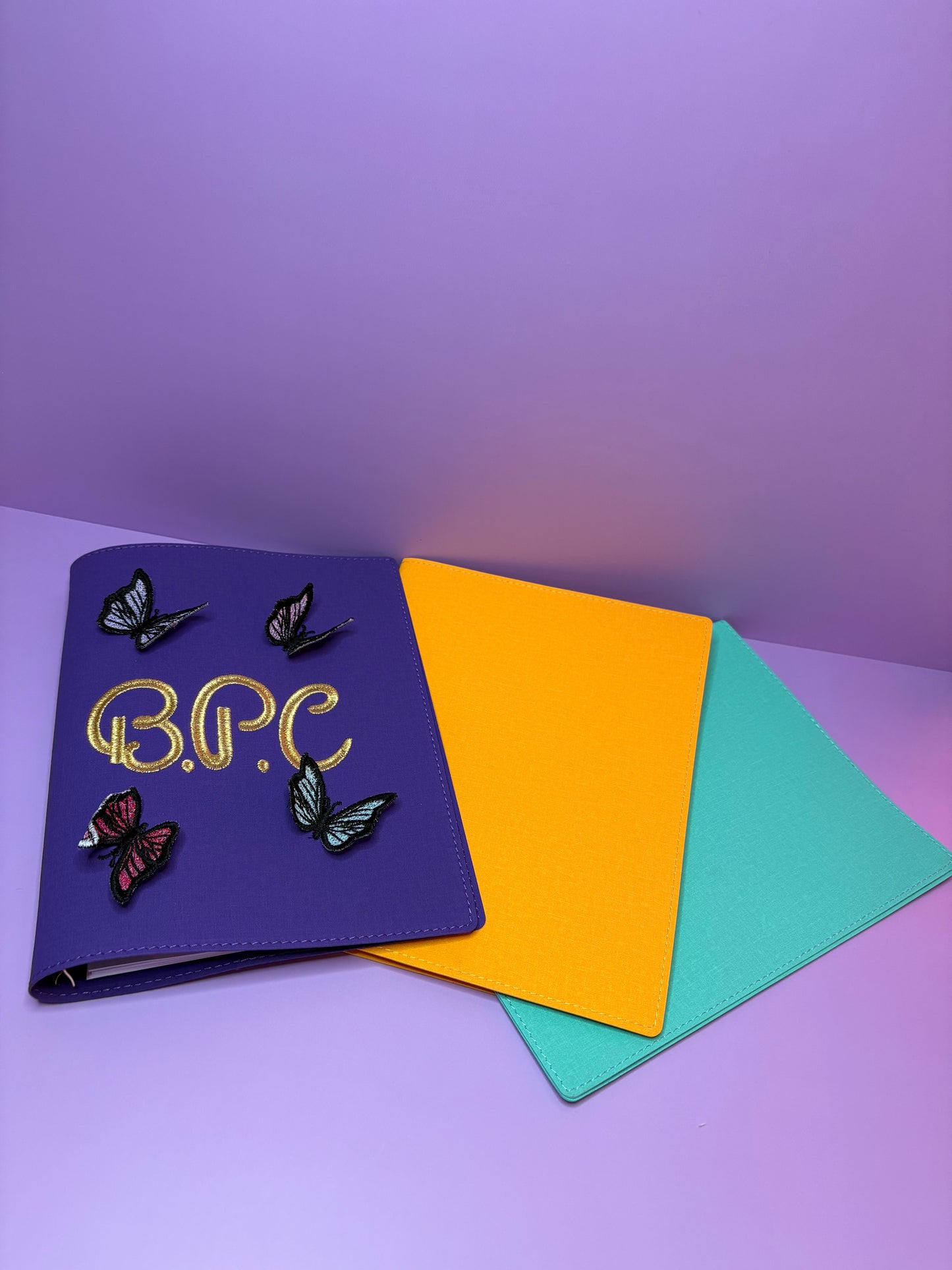 3D butterfly embroidered personalised A5 fabric file notebook in purple with yellow and aqua covers displayed on a purple background
