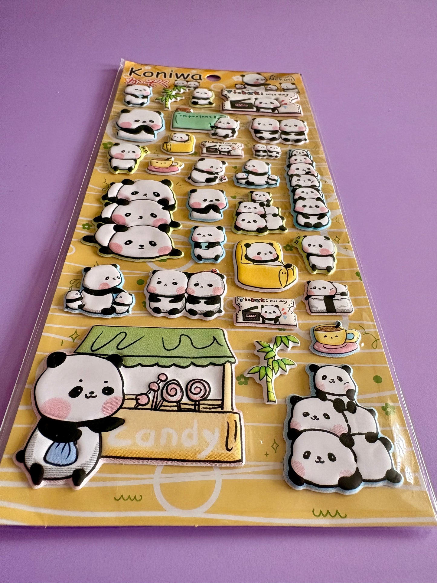 A sheet of cute 3D panda stickers on a yellow backing card, photographed on a solid purple background. The stickers feature various panda poses, a candy shop, and accessories.