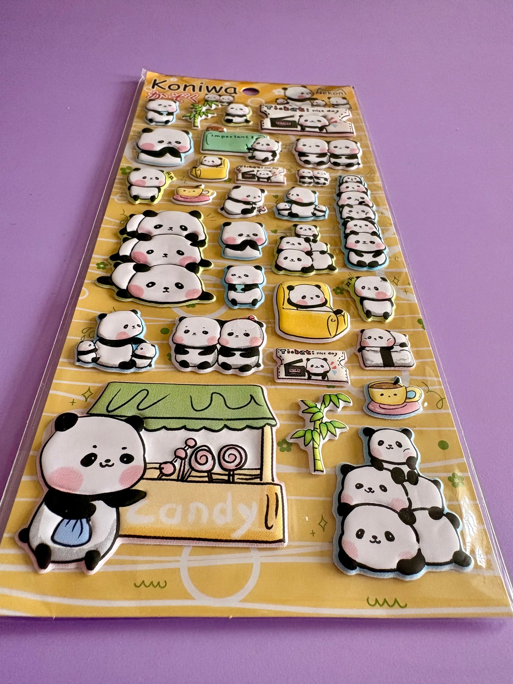 A sheet of cute 3D panda stickers on a yellow backing card, photographed on a solid purple background. The stickers feature various panda poses, a candy shop, and accessories.