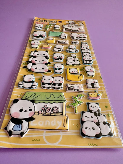 A sheet of cute 3D panda stickers on a yellow backing card, photographed on a solid purple background. The stickers feature various panda poses, a candy shop, and accessories.