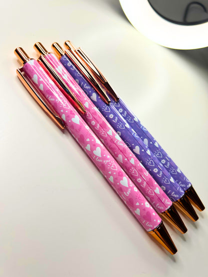 Set of kawaii luxe metal ballpoint pens in pink and purple with heart designs and rose gold accents.