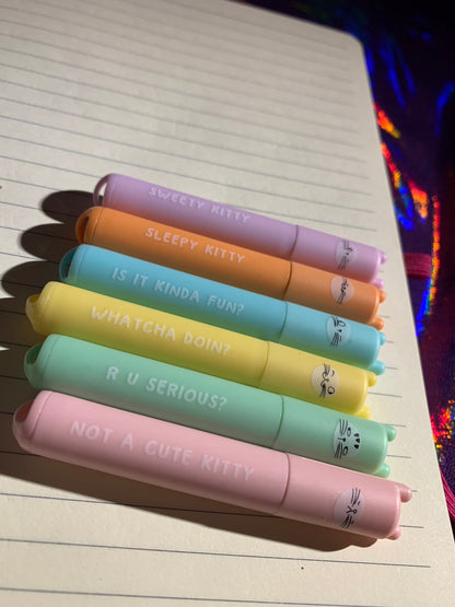 Cute cat-themed mini highlighters in bright colors on notebook.