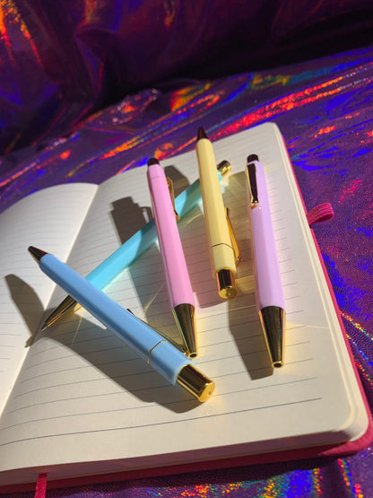 Pastel paradise pen set with gold trim on open notebook, blue ink stationery.